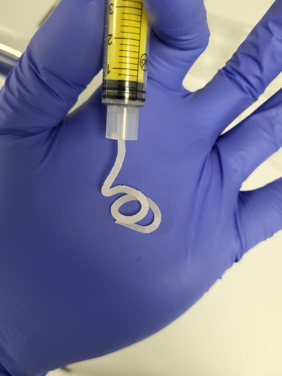 Close-up of biofabricated material from a syringe in a gloved hand